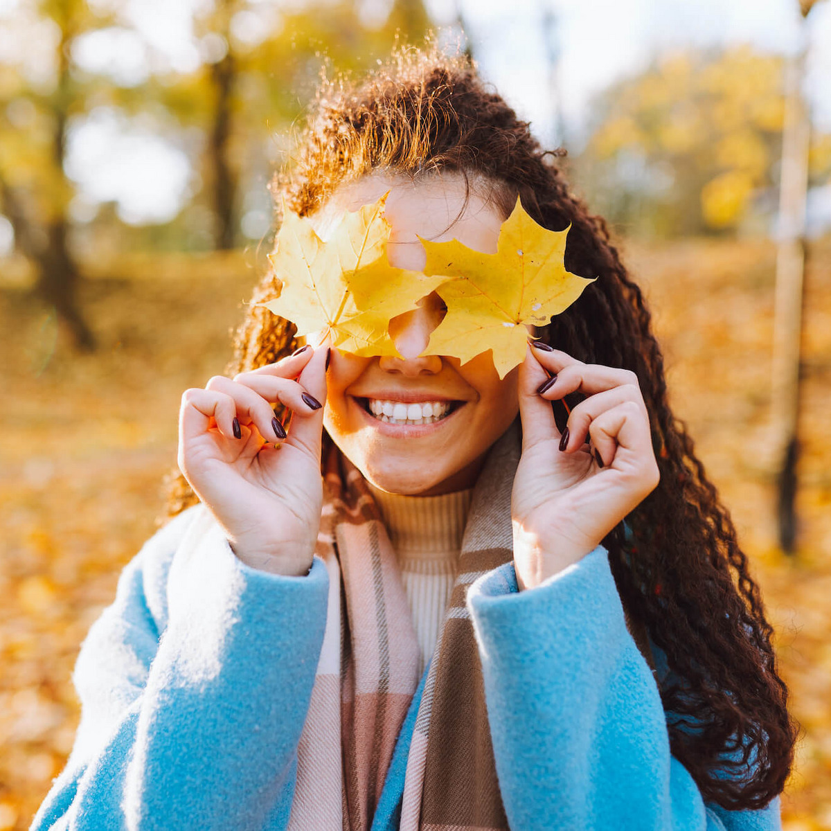 Junge Frau in einem herbstlichen Park hält sich bunte Blätter vor die Augen