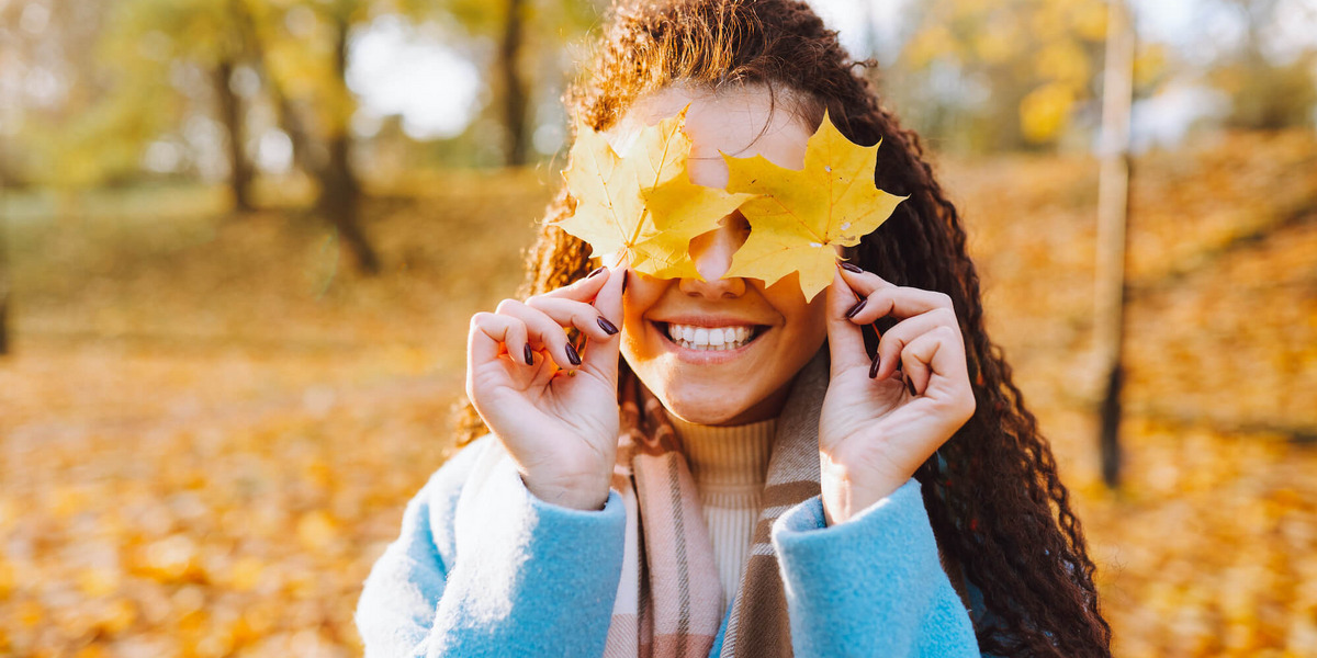 Junge Frau in einem herbstlichen Park hält sich bunte Blätter vor die Augen