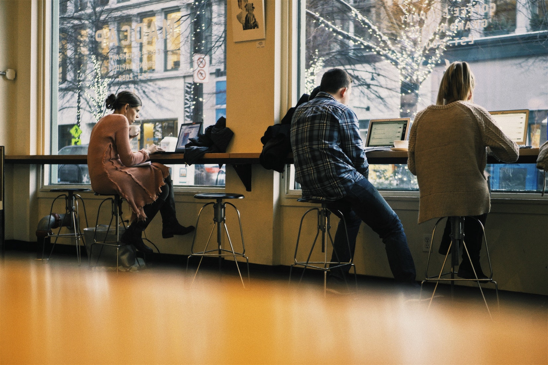Drei Menschen sitzen am Thresen eines Cafes und arbeiten an Laptops.