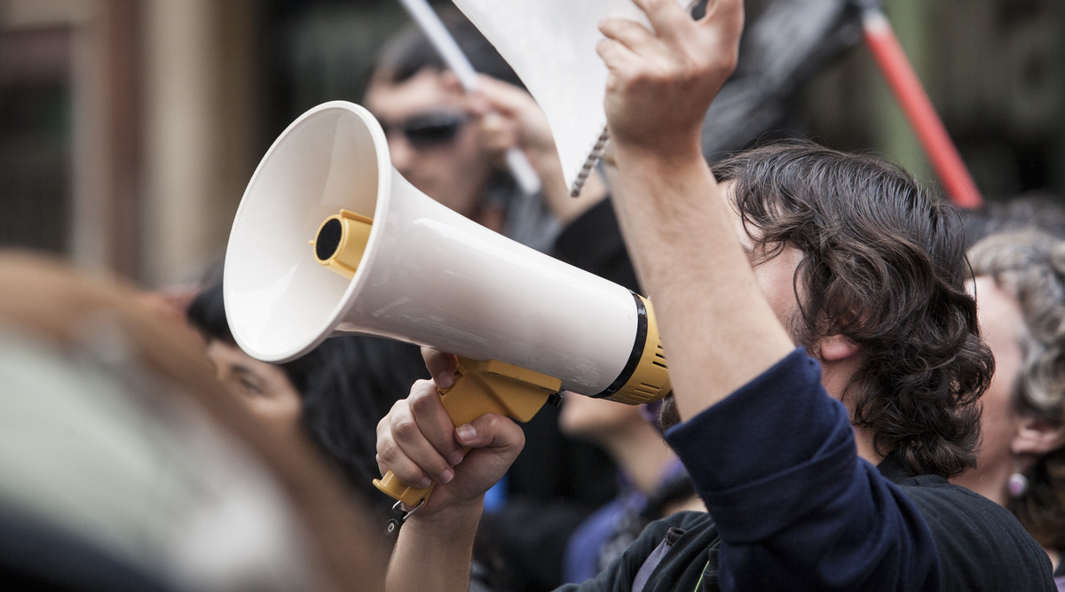 Ein junger Mann ruft auf einer Demo in ein Megafon