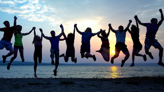 Jugendliche halten sich an den Händen und springen vor einem Sonnenuntergang hoch.