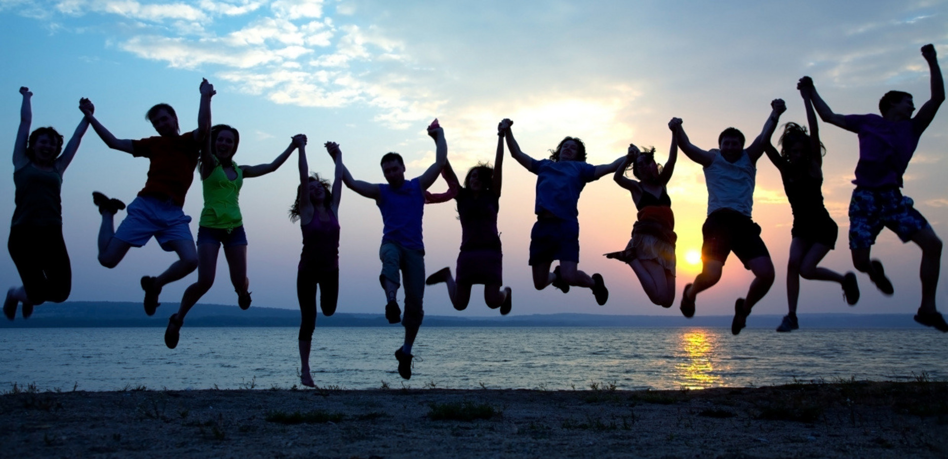 Jugendliche halten sich an den Händen und springen vor einem Sonnenuntergang hoch.
