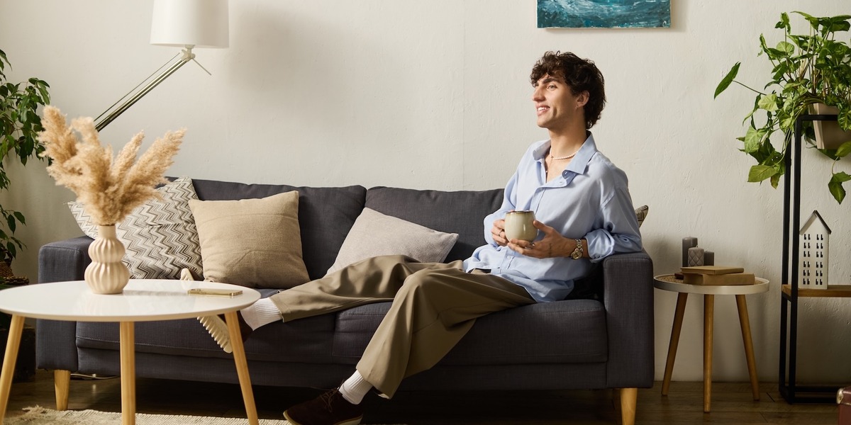Eine Person sitzt entspannt mit einer Tasse in der Hand auf einem Sofa in einem hellen Wohnzimmer.