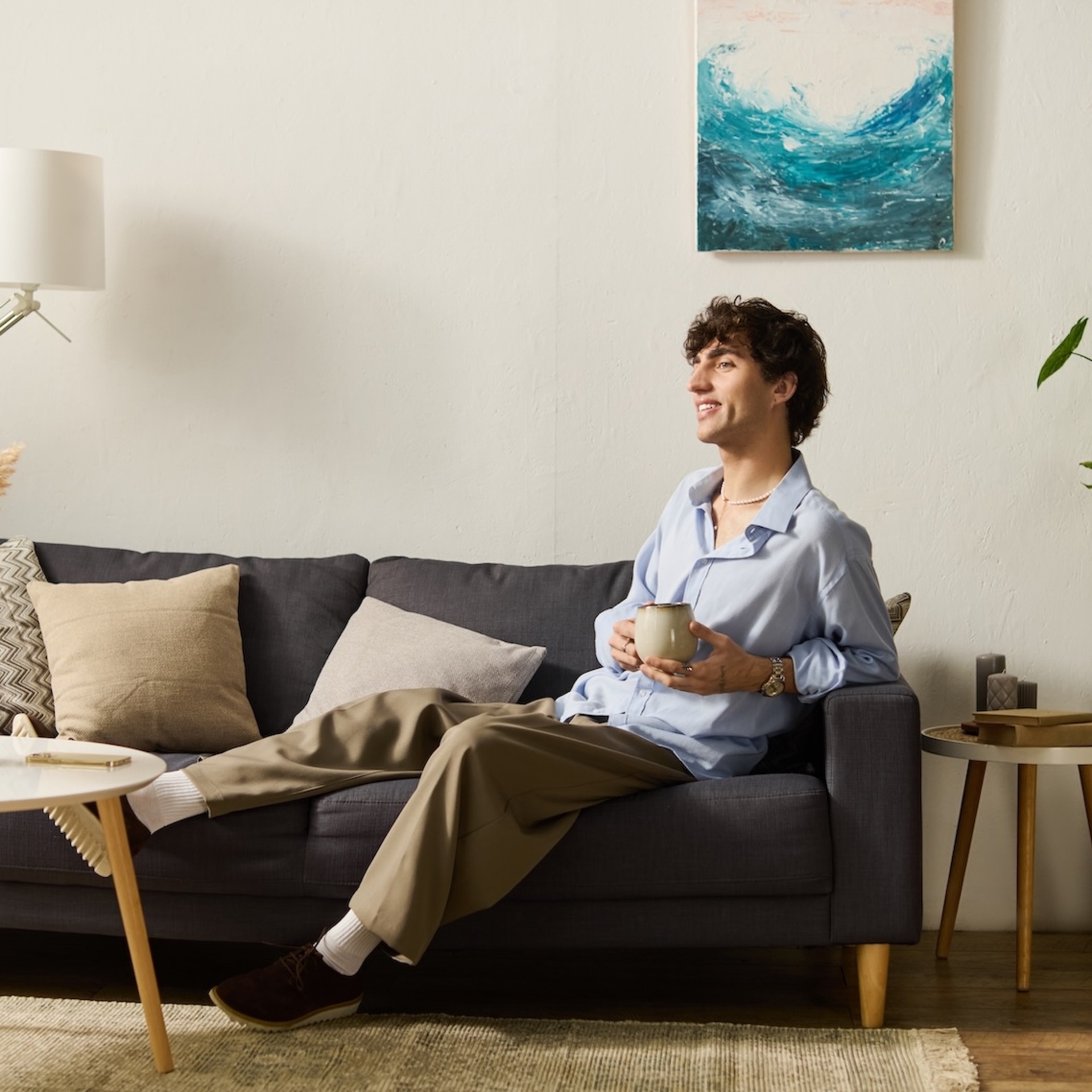 Eine Person sitzt entspannt mit einer Tasse in der Hand auf einem Sofa in einem hellen Wohnzimmer.