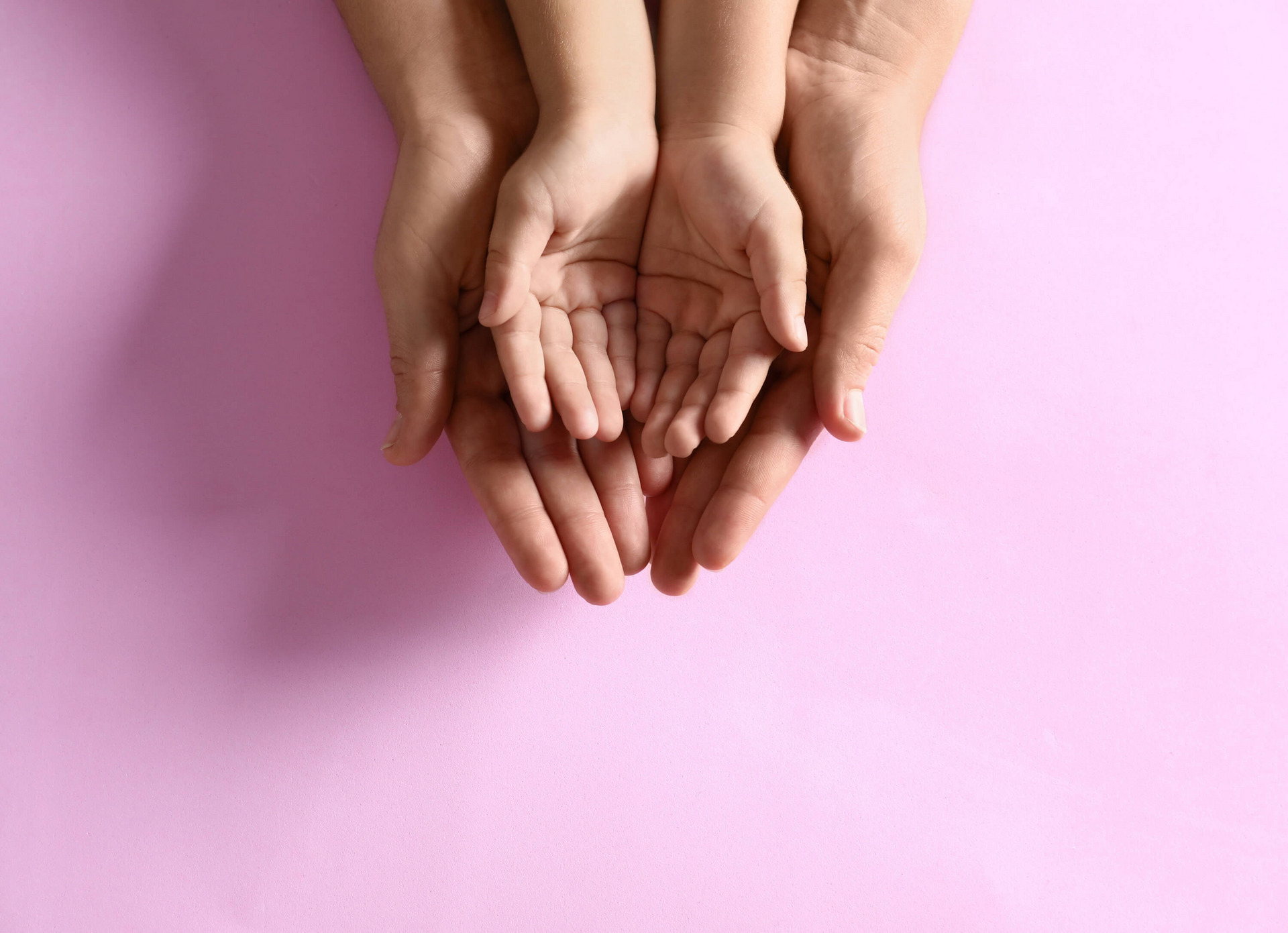 Kinderhände liegen in größeren Händen auf rosa Hintergrund