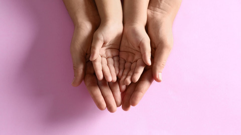 Kinderhände liegen in größeren Händen auf rosa Hintergrund