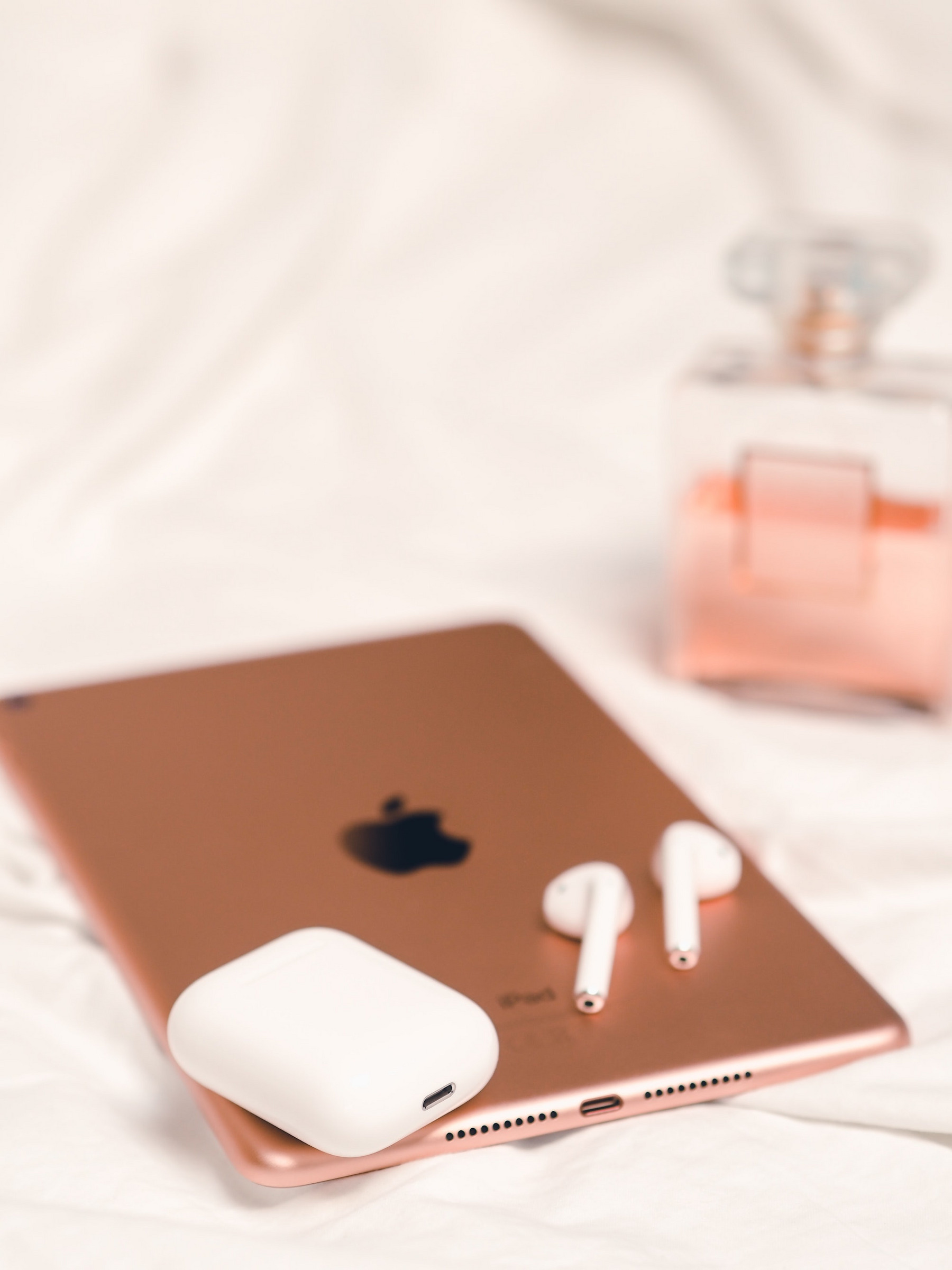 Apple Earpods-Kopfhörer liegen auf einem rotgoldenen iPad, im Hintergrund steht ein Parfumflacon.