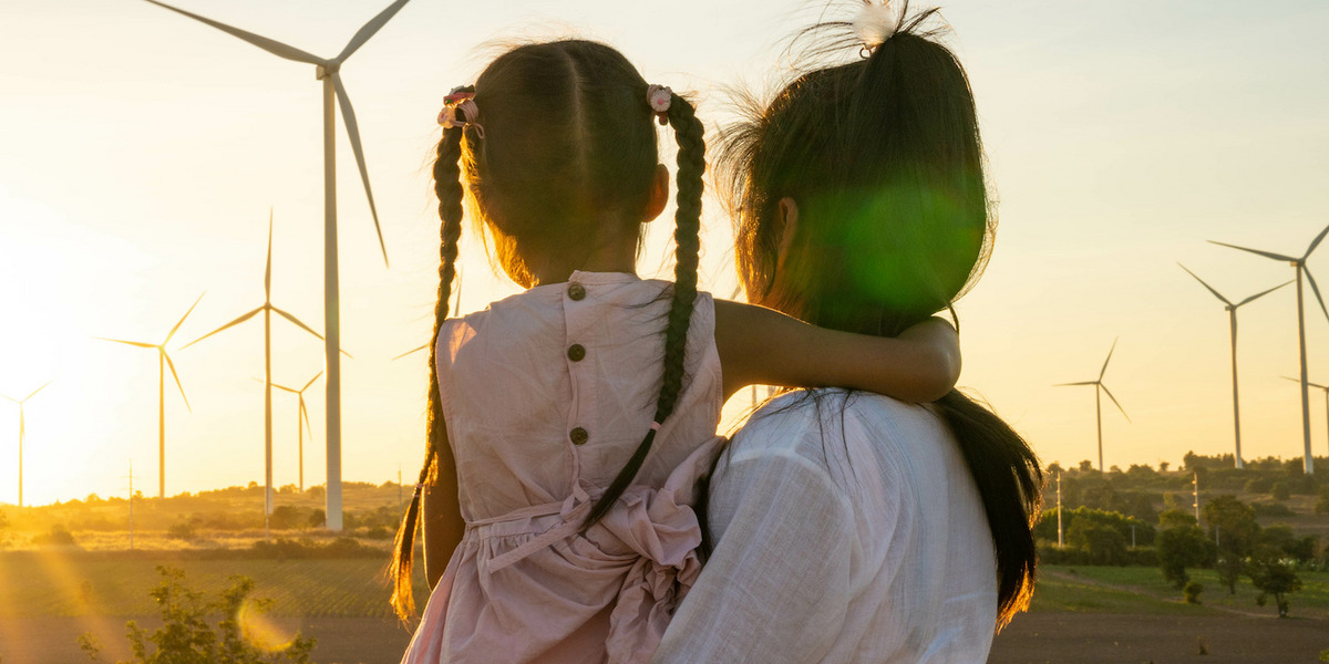 Im Vordergrund eine Frau mit einem kleinen Mädchen auf dem Arm, im Hintergrund ein Feld mit Windmühlen.