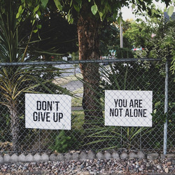 Drei Schilder mit den Sprüchen "Don't give up","You are not alone" und "You matter" vor ein paar Büschen.