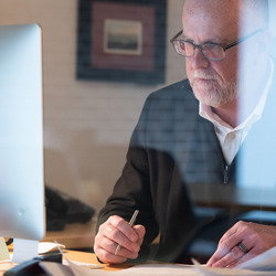 Ein Mann mit Brille sitzt vor seinem Computer mit einem Stift in der Hand.