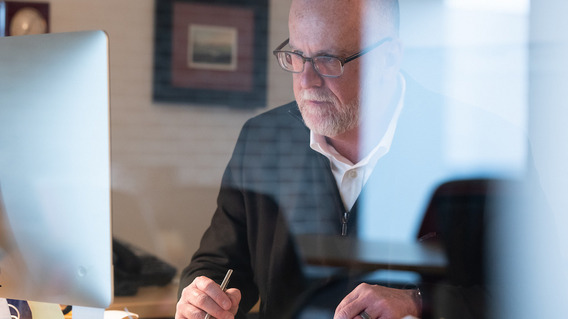 Ein Mann mit Brille sitzt vor seinem Computer mit einem Stift in der Hand.