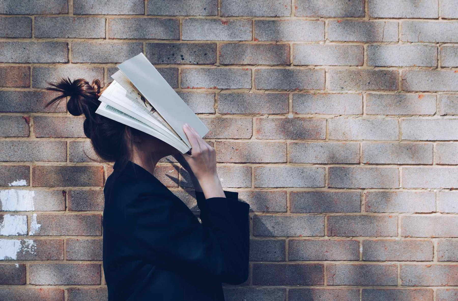 Eine junge Frau schlägt sich genervt ein Buch vor das Gesicht.