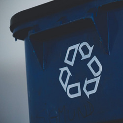 Eine blaue Mülltonne, auf die das Recyclingsymbol gedruckt ist, drei ineinander übergehende Pfeile, die den Verwertungskreislauf widerspiegeln sollen