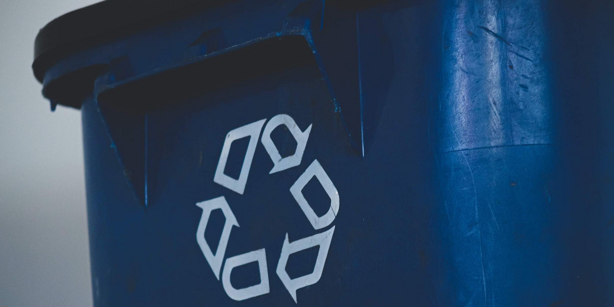 Eine blaue Mülltonne, auf die das Recyclingsymbol gedruckt ist, drei ineinander übergehende Pfeile, die den Verwertungskreislauf widerspiegeln sollen