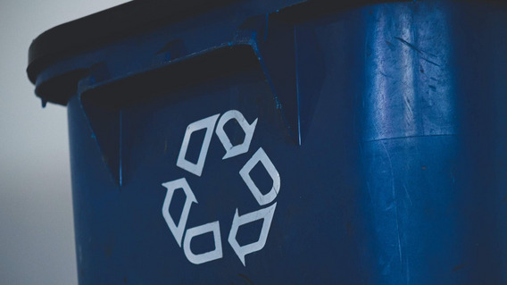 Eine blaue Mülltonne, auf die das Recyclingsymbol gedruckt ist, drei ineinander übergehende Pfeile, die den Verwertungskreislauf widerspiegeln sollen