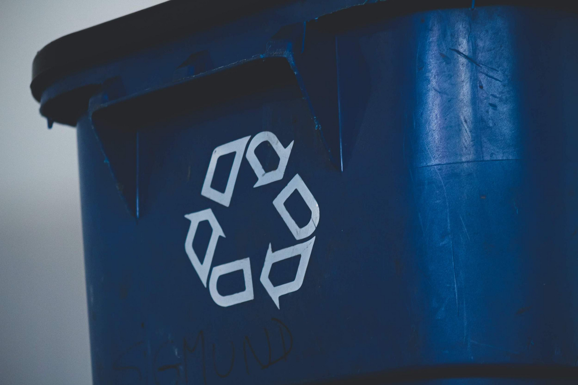 Eine blaue Mülltonne, auf die das Recyclingsymbol gedruckt ist, drei ineinander übergehende Pfeile, die den Verwertungskreislauf widerspiegeln sollen