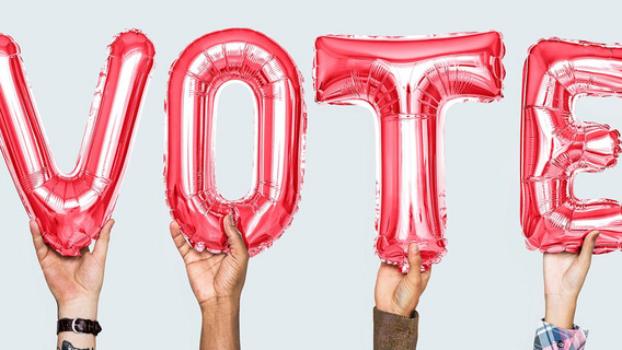 Vier Hände halten die englische Aufforderung „VOTE“ („Stimme ab“) in Ballonbuchstaben in die Luft