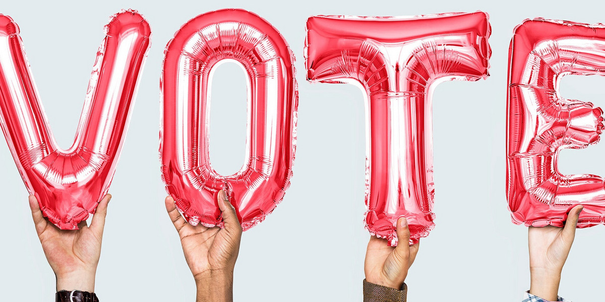 Vier Hände halten die englische Aufforderung „VOTE“ („Stimme ab“) in Ballonbuchstaben in die Luft