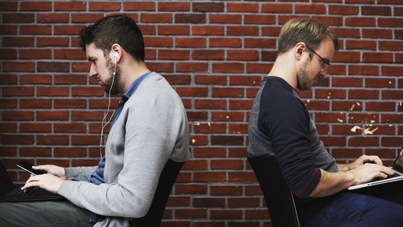 Zwei Männer sitzen mit dem Rücken zueinander und arbeiten an Laptops.