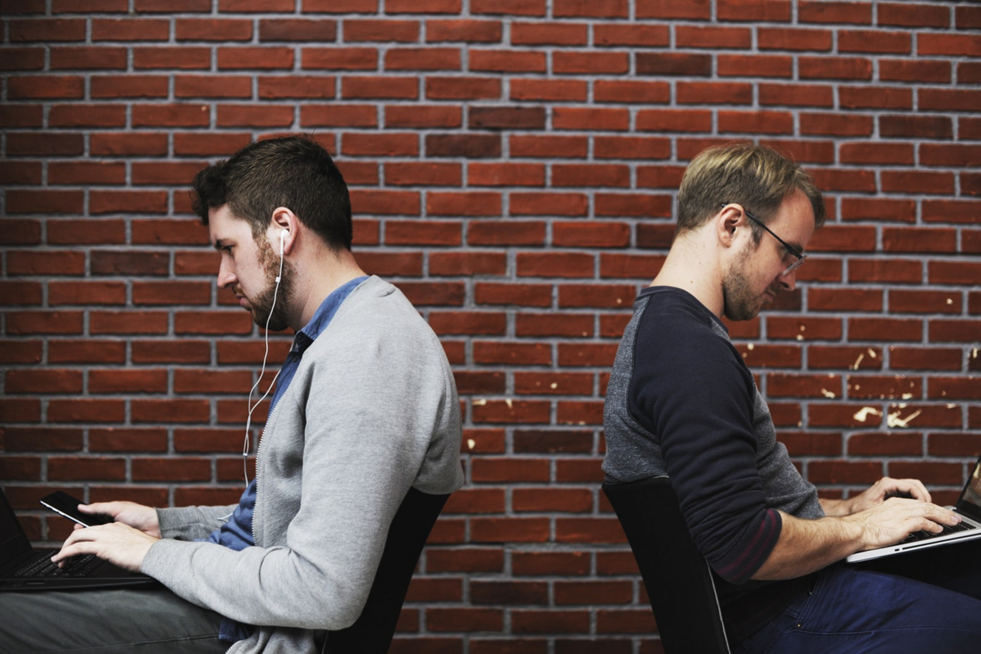 Zwei Männer sitzen mit dem Rücken zueinander und arbeiten an Laptops.