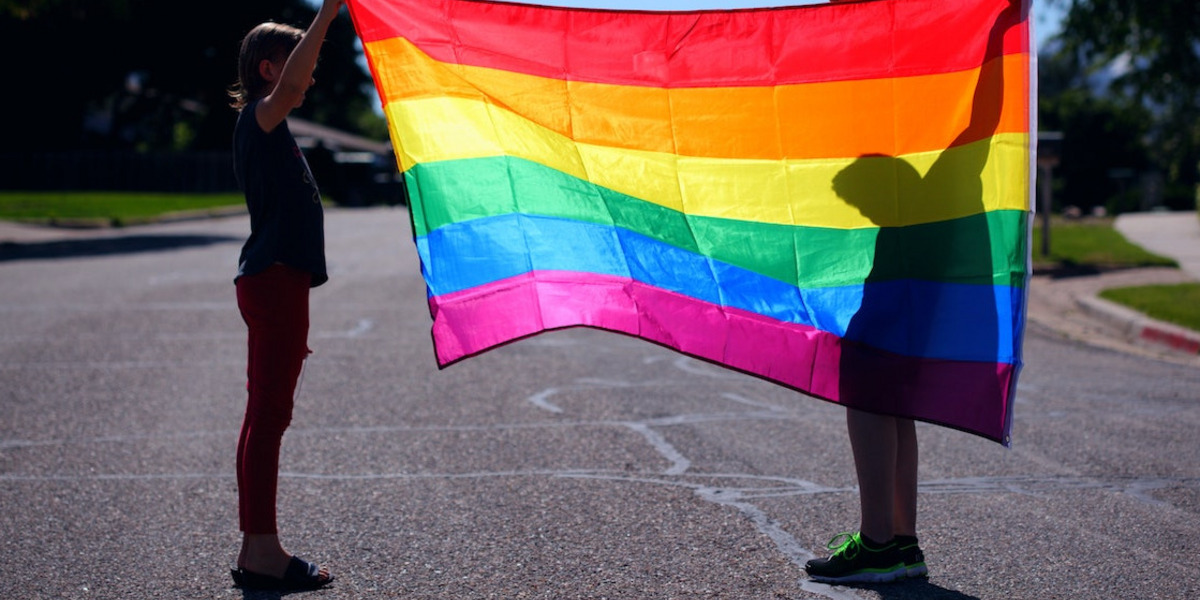 Zwei Personen halten eine Prideflagge hoch.