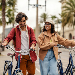 Ein junger Mann läuft gemeinsam mit einer jungen Frau auf einem Weg. Beide schieben ihr Fahrrad.
