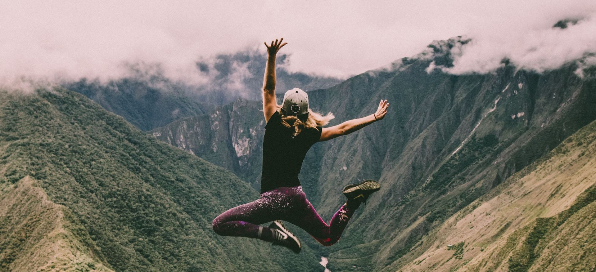 Eine Frau springt vor einer grünen Bergkulisse in Peru fröhlich in die Luft