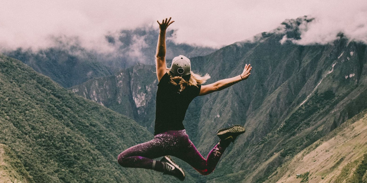 Eine Frau springt vor einer grünen Bergkulisse in Peru fröhlich in die Luft
