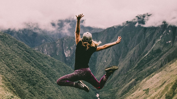 Eine Frau springt vor einer grünen Bergkulisse in Peru fröhlich in die Luft