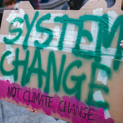 Eine Person hält ein Schild mit dem Text "System change, not climate change"