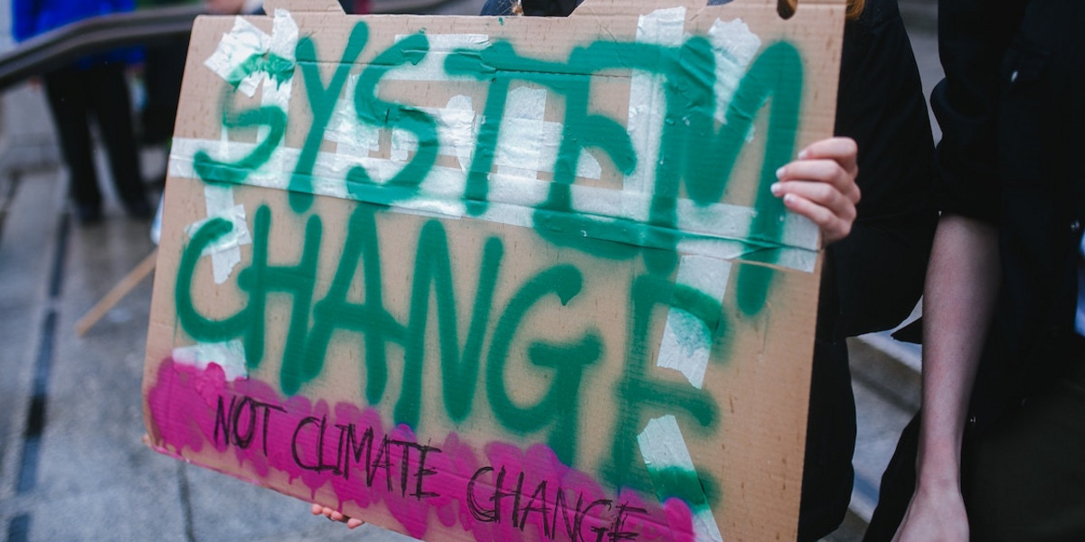 Eine Person hält ein Schild mit dem Text "System change, not climate change"