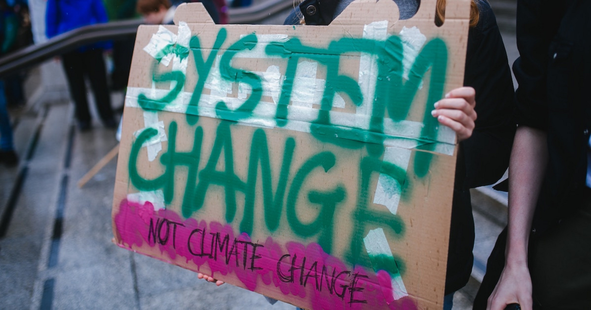 Eine Person hält ein Schild mit dem Text "System change, not climate change"