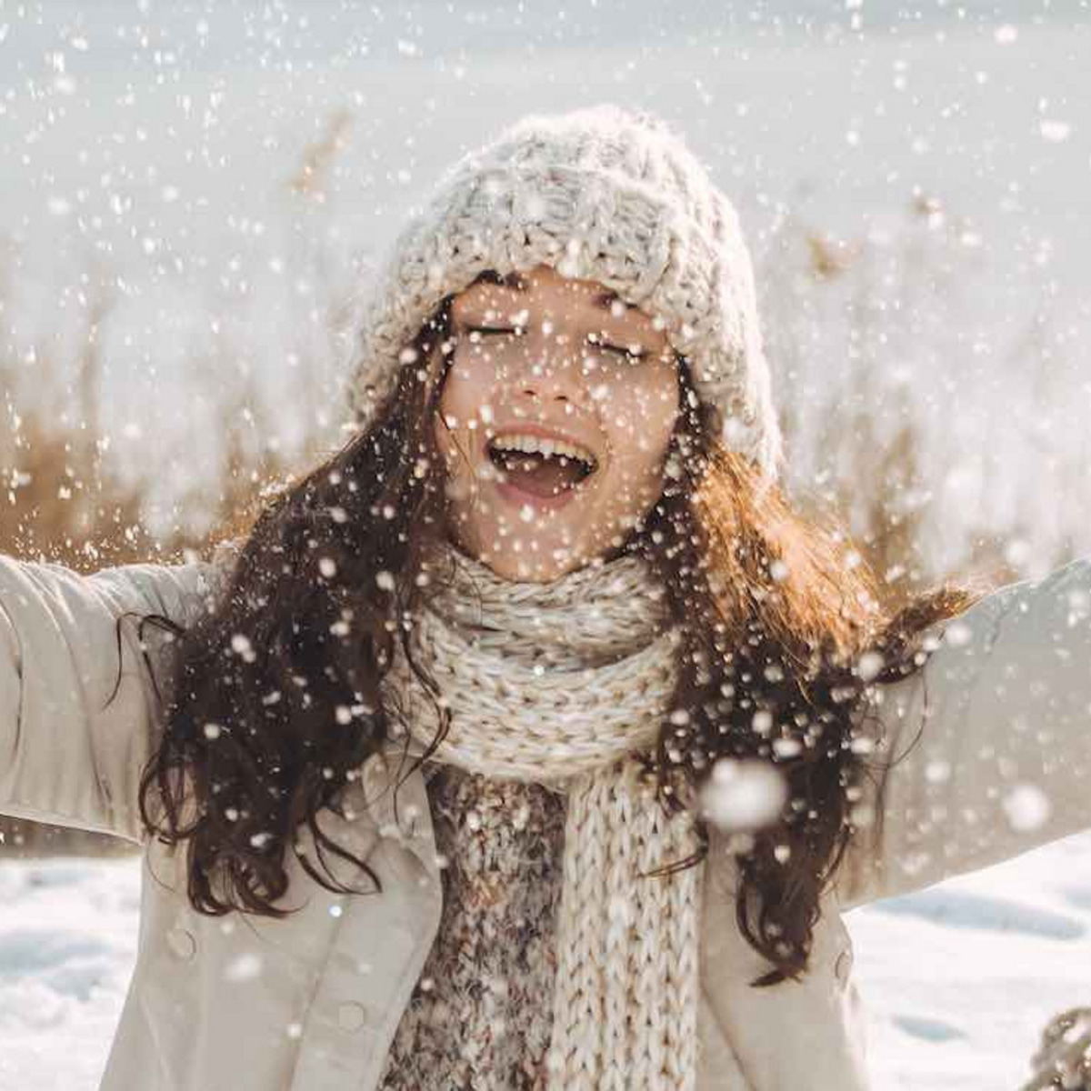 Eine junge, glückliche Frau sitzt in einer Schneelandschaft. Hinter ihr steht ein Schlitten auf dem Boden.