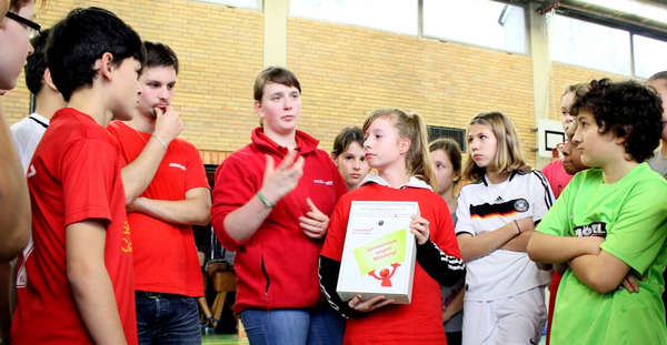 Schüler in einer Turnhalle halten einen Kummerkasten gegen Mobbing