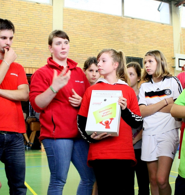Schüler in einer Turnhalle halten einen Kummerkasten gegen Mobbing