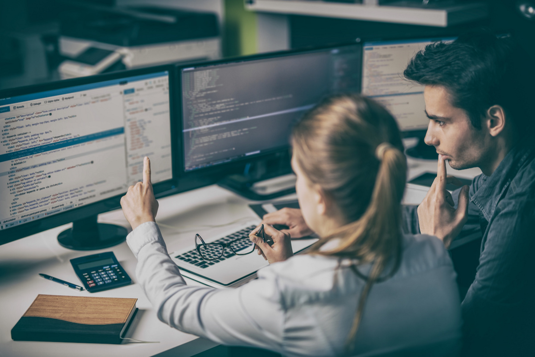 Eine Frau und ein Mann sitzen vor Computerbildschirmen.