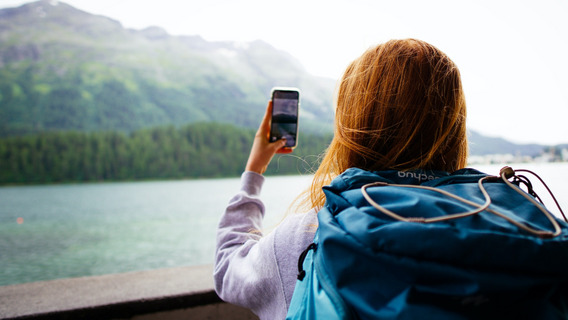 Eine junge Frau steht vor einer Bergkulisse und macht ein Foto