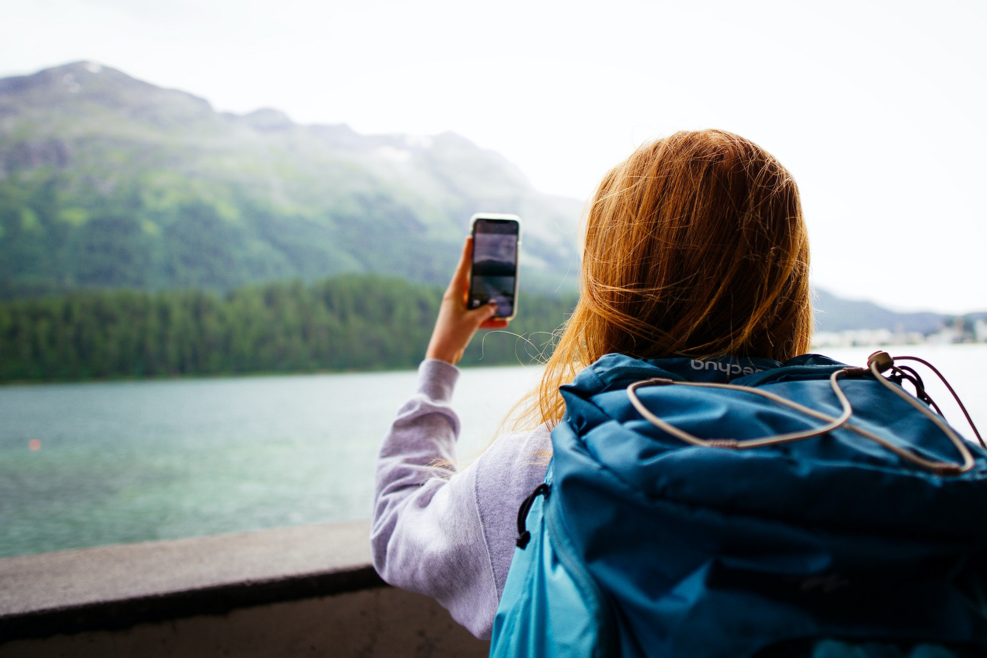 Eine junge Frau steht vor einer Bergkulisse und macht ein Foto