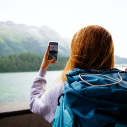 Eine junge Frau steht vor einer Bergkulisse und macht ein Foto