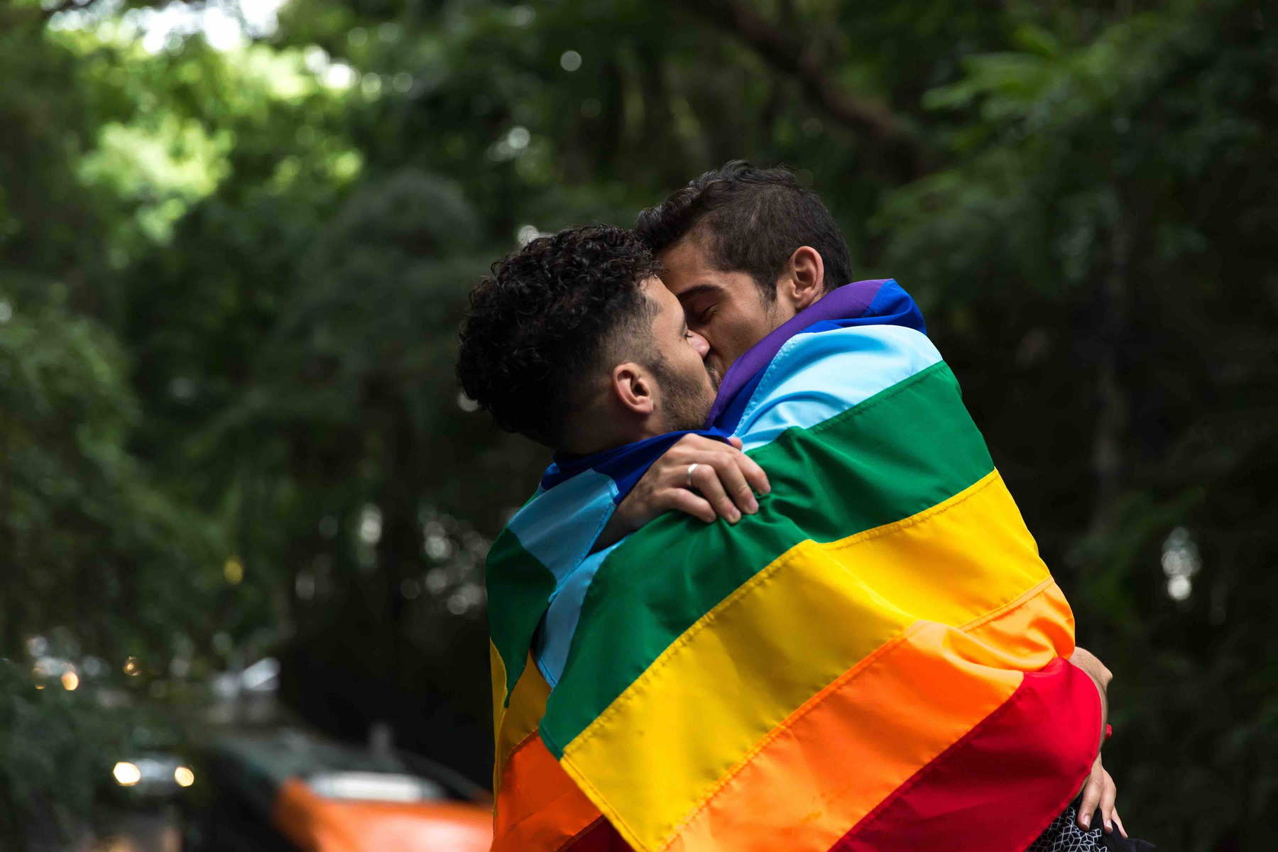 Zwei Personen küssen sich unter einer Pride-Flagge