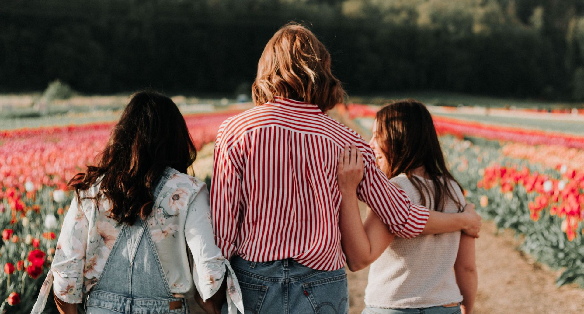 Drei junge Frauen stehen vor einem Tulpenfeld und reden vertieft miteinander.