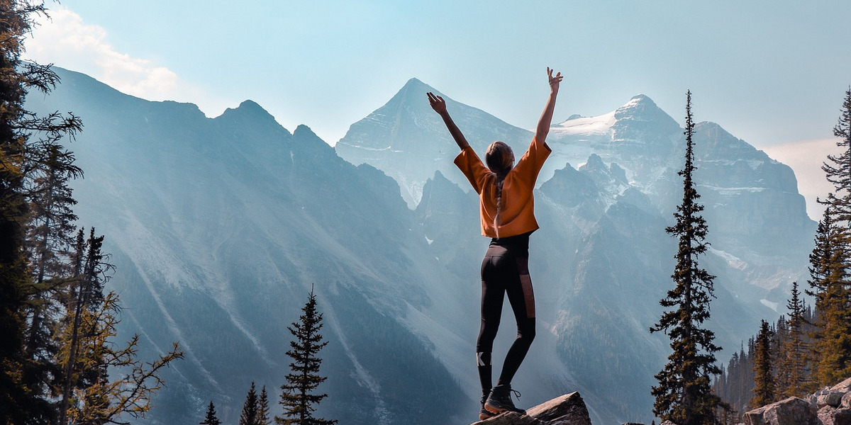 Eine junge Frau steht auf einem Berg und streckt die Arme in die Höhe.