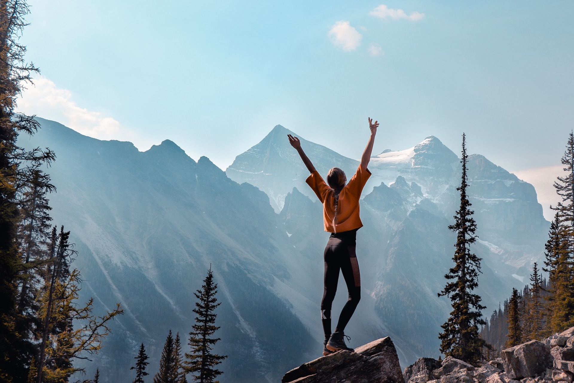 Eine junge Frau steht auf einem Berg und streckt die Arme in die Höhe.