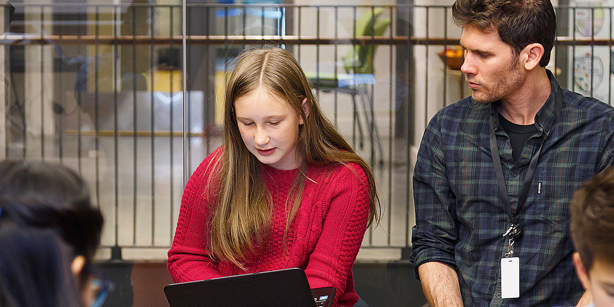 Eine Schülerin schaut gemeinsam mit ihrem Lehrer auf einen Laptop.