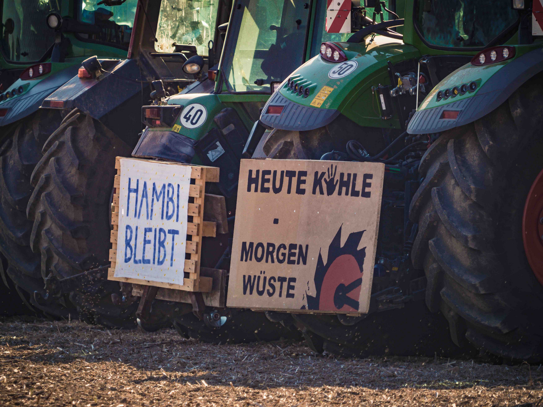 Traktoren und zwei Schilder mit Text: "Hambi bleibt" / "Heute Kohle – Morgen Wüste"