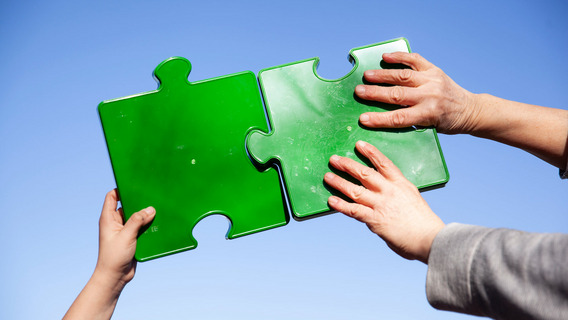 Zwei Personen fügen große grüne Puzzleteile zusammen