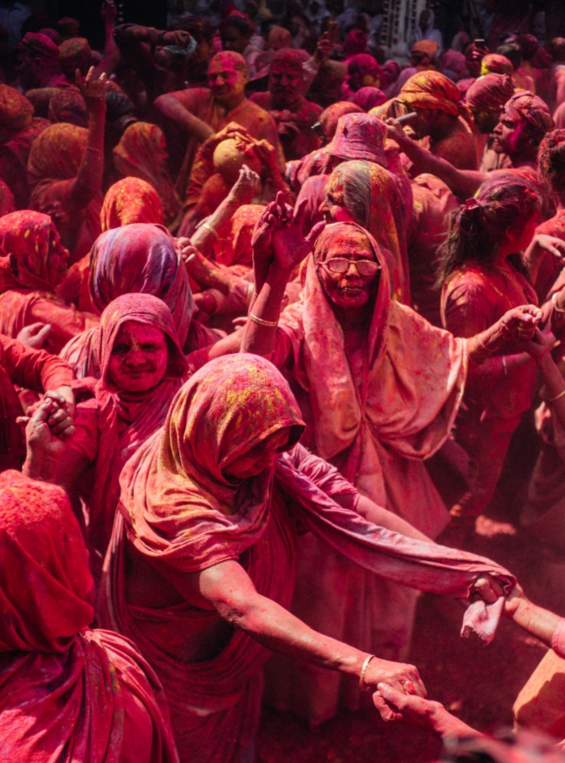 Das Bild zeigt in farbigen Staub getauchte Frauen. Im Hinduismus gilt, dass Frauen nach dem Tod ihrer Ehemänner auf irdische Freuden verzichten müssen. So ist das Feiern von Holi für hinduistische Witwen seit 400 Jahren verboten. Aber seit einigen Jahren organisiert die NGO Sulabh International in Vrindavan ein Treffen speziell für verwitwete Frauen, um ihnen die Teilnahme an Holi ermöglichen zu können.