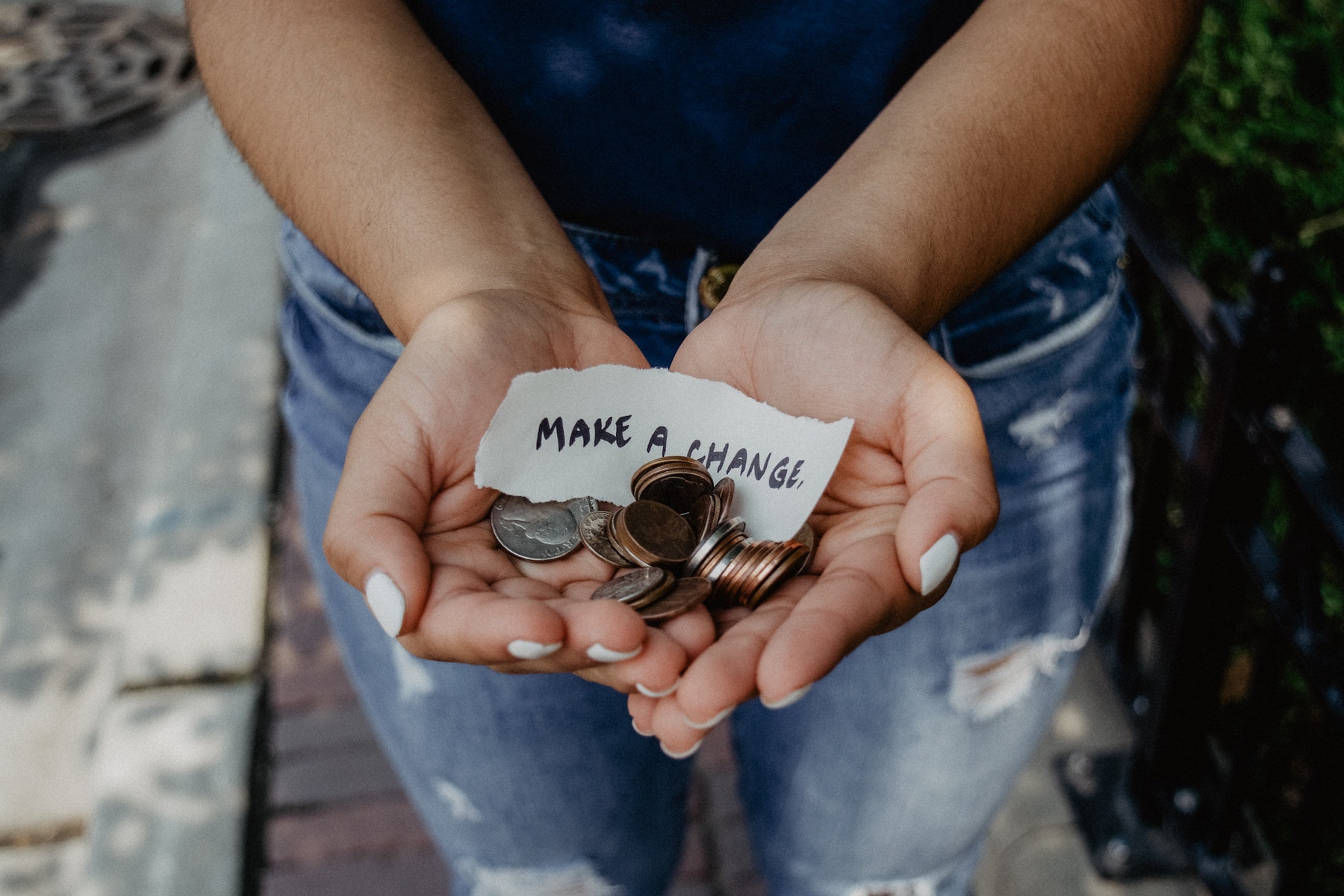 Eine Frau hält Münzen in den aufgebreiteten Händen und hält sie uns hin. In ihren Händen liegt auch ein Zettel auf dem steht: "Make a change."