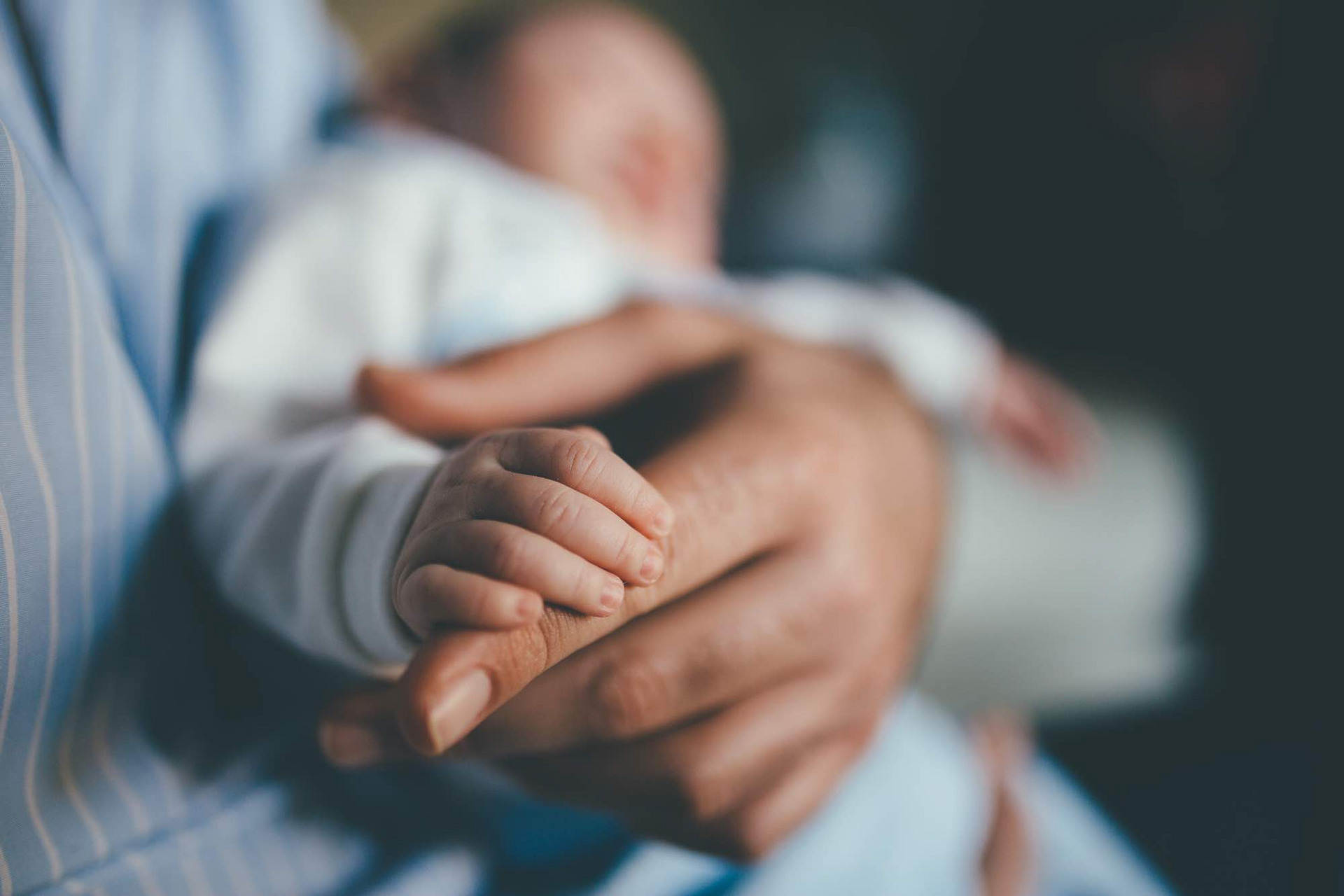 Eine Babyhand umfasst den Finger eines Erwachsenen.