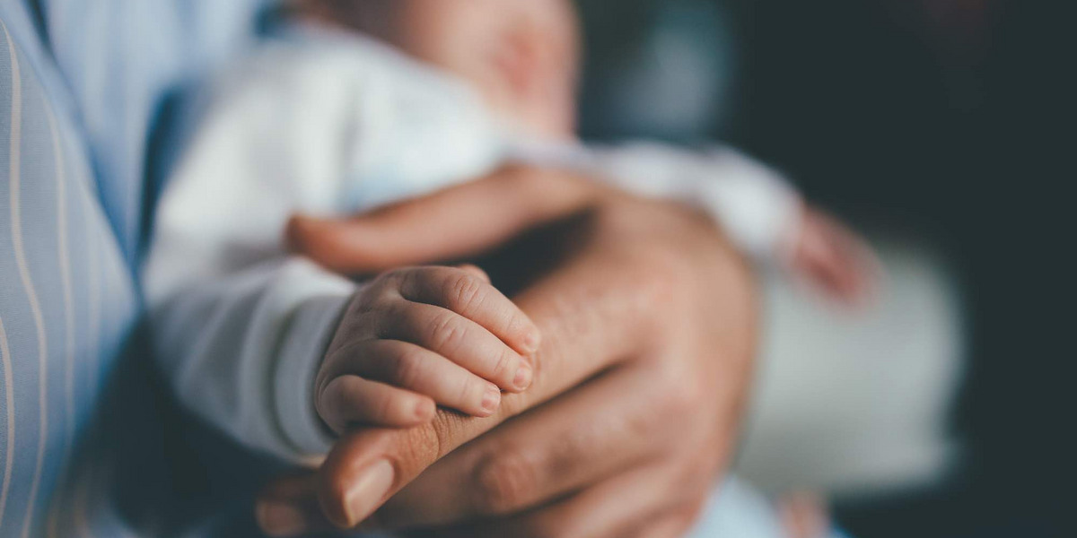 Eine Babyhand umfasst den Finger eines Erwachsenen.